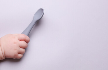 Baby hand holding silicone feeding spoon on gray background