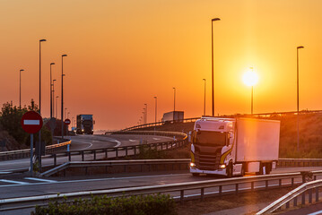 Several trucks driving through a multi-level highway interchange at sunrise.