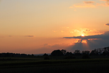 A captivating sunset over a rural landscape, casting a warm and serene glow. Sunrays pierce through...