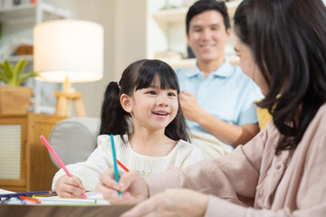 Asian mother and daughter happily sit together in the living room, drawing pictures and enjoying...