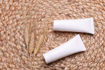 Cream tubes with dry wheat ears on a wicker mat. Natural cosmetic. Beauty concept