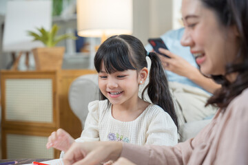 Asian mother and daughter happily sit together in the living room, drawing pictures and enjoying...
