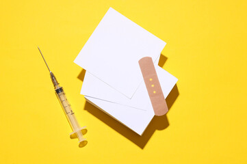Medical Adhesive bandage plaster with syringe and white cards on yellow background