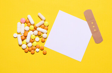White card and Medical Adhesive bandage plasters, pills on yellow background. Top view