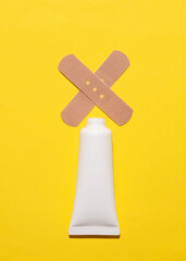 Bottle of cream with medical plaster on yellow background