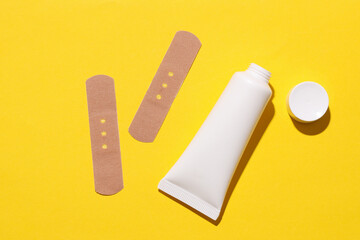 Bottle of cream with medical plaster on yellow background