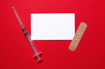 Medical Adhesive bandage plaster with syringe and white card on red background