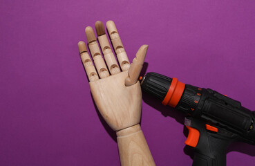 Wooden hand of a puppet and a cordless screwdriver on a purple background. Repair concept