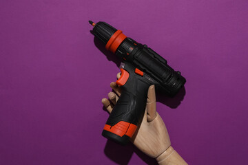 Wooden hand of puppet holding cordless screwdriver on purple background