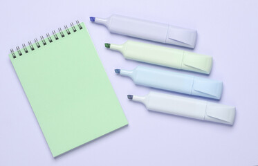 Markers or colored felt-tip pens with notebook on purple pastel background. Creative layout