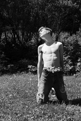 A shirtless young man kneels in the grass, wearing jeans decorated with flowers.