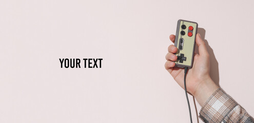 Man's hand in shirt holding retro joystick on beige pastel background with shadow. Vintage video game. Copy space for your text © splitov27