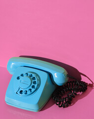 Rotary retro rotary telephone painted in blue paint on a pink wall background. Creative layout