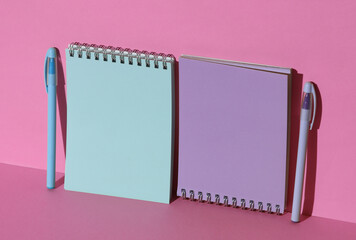 Blue and purple notebooks with pens on pink background with shadow. Creative layout