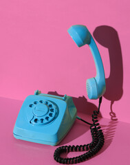 Rotary retro rotary telephone with a floating handset painted in blue paint on pink background with shadow. Creative layout