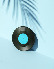 Obraz premium Vinyl record on blue background with palm leaf shadow. Minimalism. Retro 80s creative layout
