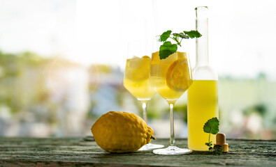 Limoncello liqueur with ice cubes in glasses and a ripe lemon on rustic wooden table.Traditional...
