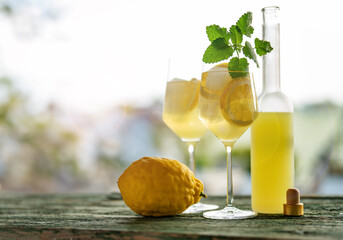 Limoncello liqueur with ice cubes in glasses and a ripe lemon on rustic wooden table.Traditional...
