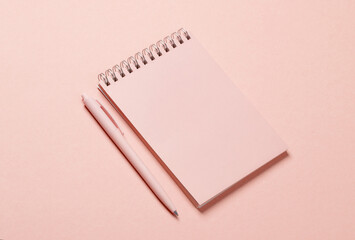 Pink notebook with a pen on pink background