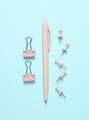 Pink stationery accessories on blue background. Pen, paper clips, pins. Flat lay. Top view