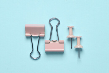 Pink paper clip holders and pins on a blue background. Minimalism
