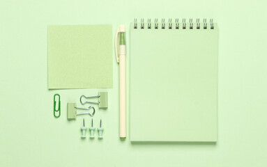 Green stationery accessories on green pastel background. Notepad, memo papers, pen, paper clips, pins. Monochrome objects. Flat lay. Top view