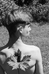A shirtless young man outdoors with a large leaf placed on his back