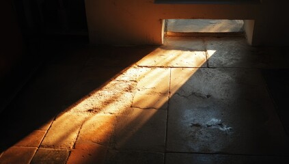 Sunlight streams diagonally across a tiled floor, illuminating cracks and textures