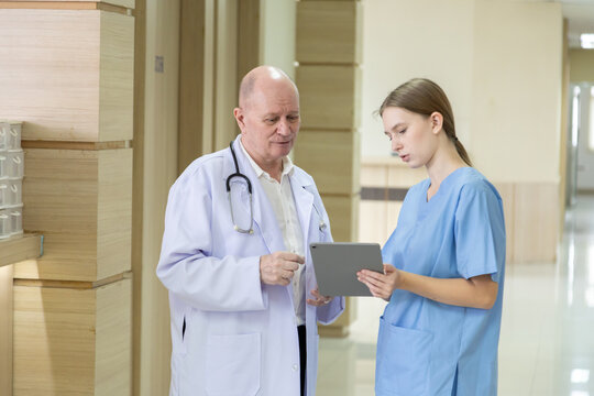 Hospital, healthcare, medical, doctor, nurse using tablet to review patient information, senior male mentoring young student trinee in hallway, technology helps improve teamwork efficiency diagnosis