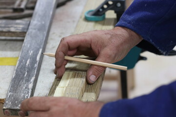 Carpenter using the pencil to mark where to cut the wood to make a recycled wood table
