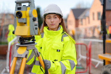 Female Construction surveyor using surveying equipment on building site while wearing bright...