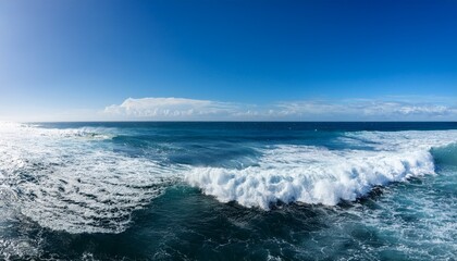 Fototapeta premium vast ocean waves crash and foam beneath a clear blue sky with distant clouds on the horizon