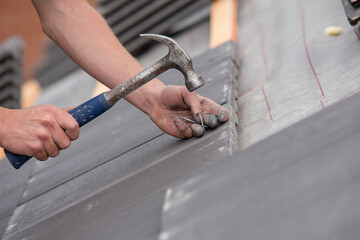 Close-up of hammering roofing tiles during renovation of residential building roof