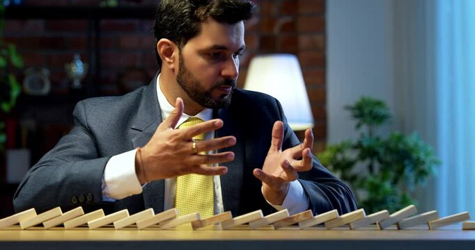 Indian businessman starting dominos effect on table, Asian corporate executive expressing frustration and stress, symbol of failure, bad decision-making, corporate pressure, and business consequences