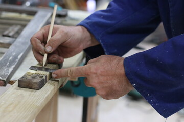 Carpenter using the pencil to mark where to cut the wood to make a recycled wood table