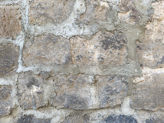 A wall made of stone and cement. The wall is grey and has a few cracks. There are some small holes in the wall