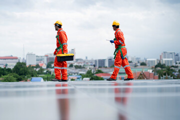 Two men in orange and green safety gear are walking on a roof