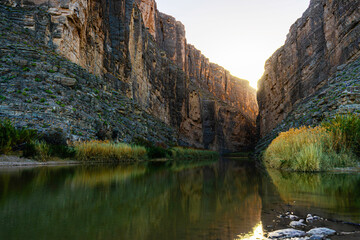 Sunlight peeks through the steep cliffs of Santa Elena Canyon at Big Bend National Park. The Rio Grande glows below, reflecting towering walls in this peaceful yet dramatic river gorge.