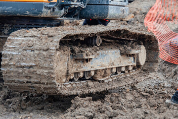 Construction worker  in bright safety gear working hard using shovel to clean tracks of his heavy...