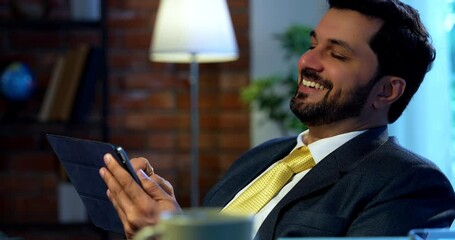 Indian businessman using tablet computer while sitting at modern office desk, Asian corporate executive multitasking with digital device, symbol of productivity, tech lifestyle, and smart working - Powered by Adobe