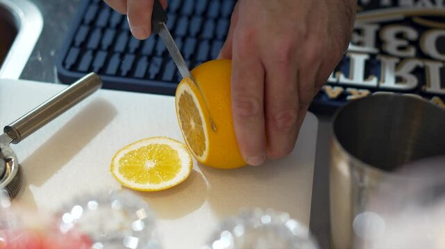 Close up of male bartender hands cutting slices of fresh lemon with small knife on bar counter. Top view of table with tools for making alcoholic drinks. Preparing ingredients for a cocktail