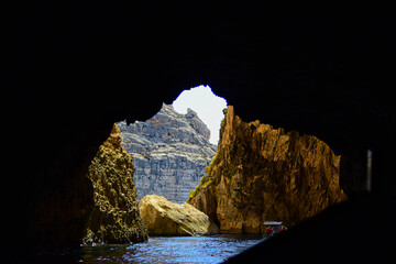 ZURRIEQ, MALTA - Augusts 06, 2021: The Blue Grotto - A famous sea cave surrounded by the deep blue sea at southern Malta. On a traditional boat surrounded by more brightly coloured boats. On a hot day