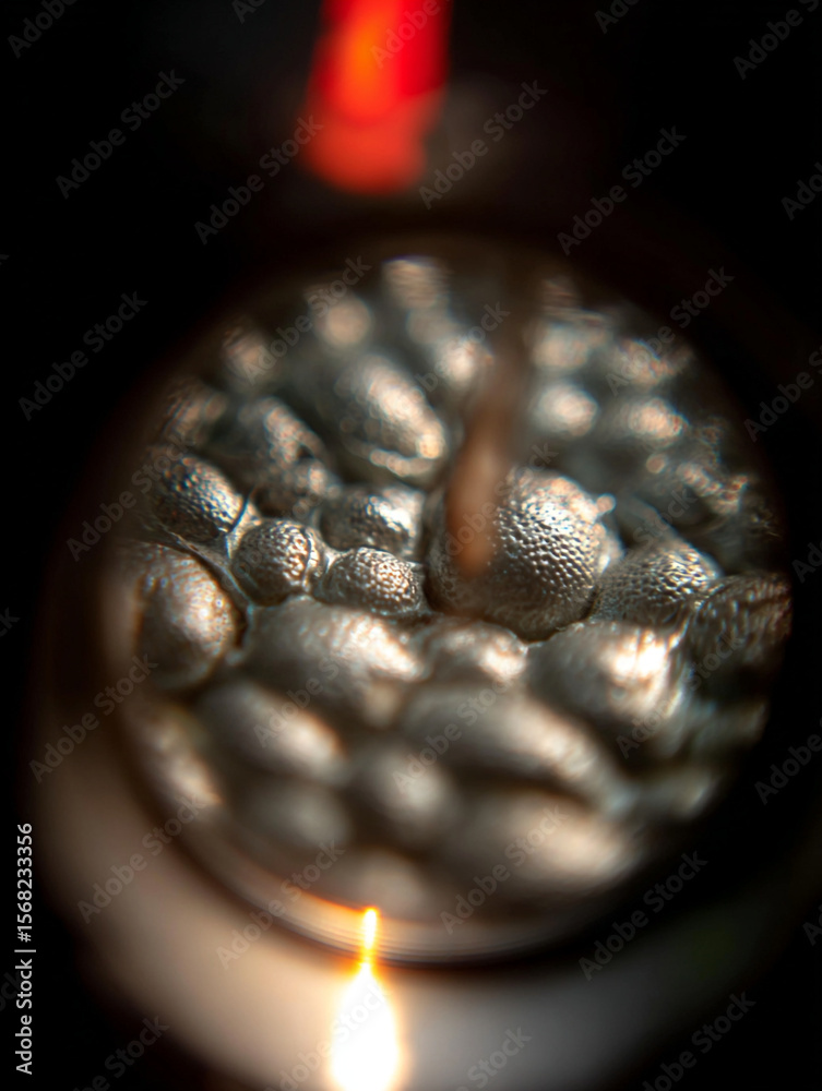 Poster a close up shot of a metallic surface with a bubble like texture and a light source at the bottom ed