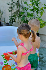 Kids play in an inflatable pool surrounded by green plants on a warm summer day.