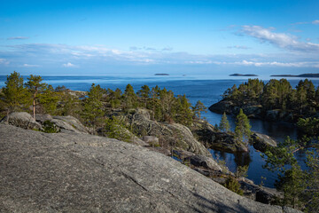 Skerries with growing trees, surrounded by the water surface of the lake against the background of a blue sky with white-blue clouds