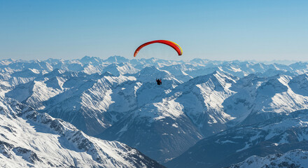 An adventurous paraglider glides high above a majestic winter mountain range under a clear sky.