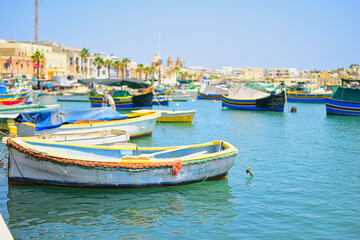 Fototapeta premium Malta Republic, Malta Island. 25.05.2023. Marsaxlokk city, The harbour and brightly coloured traditional boats on a hot sunny day.