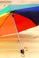 An open rainbow umbrella stands on a wooden background.