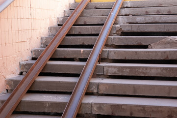 Old concrete stairs in an underpass, worn and roughly repaired. Two rusty metal rails serve as a...
