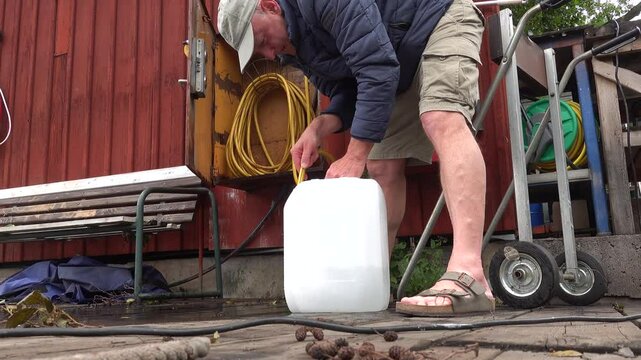 Stockholm, Sweden A man fills a plastic container with potable water on a lakeside dock with a hose.